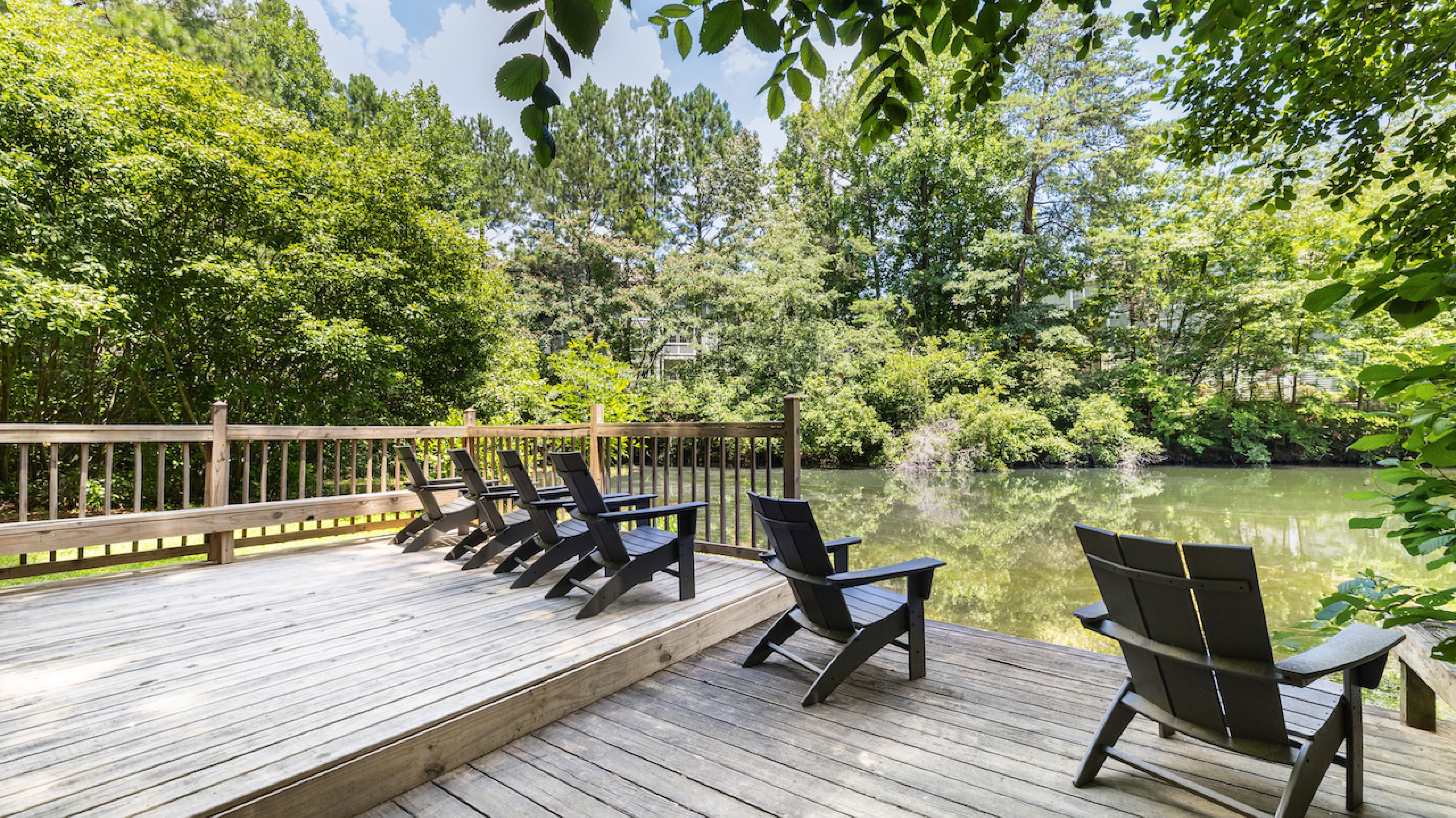 Hawthorne at Lake Heather serene lakeside deck furnished with Adirondack chairs and surrounded by lush greenery, offering a peaceful retreat by the water.