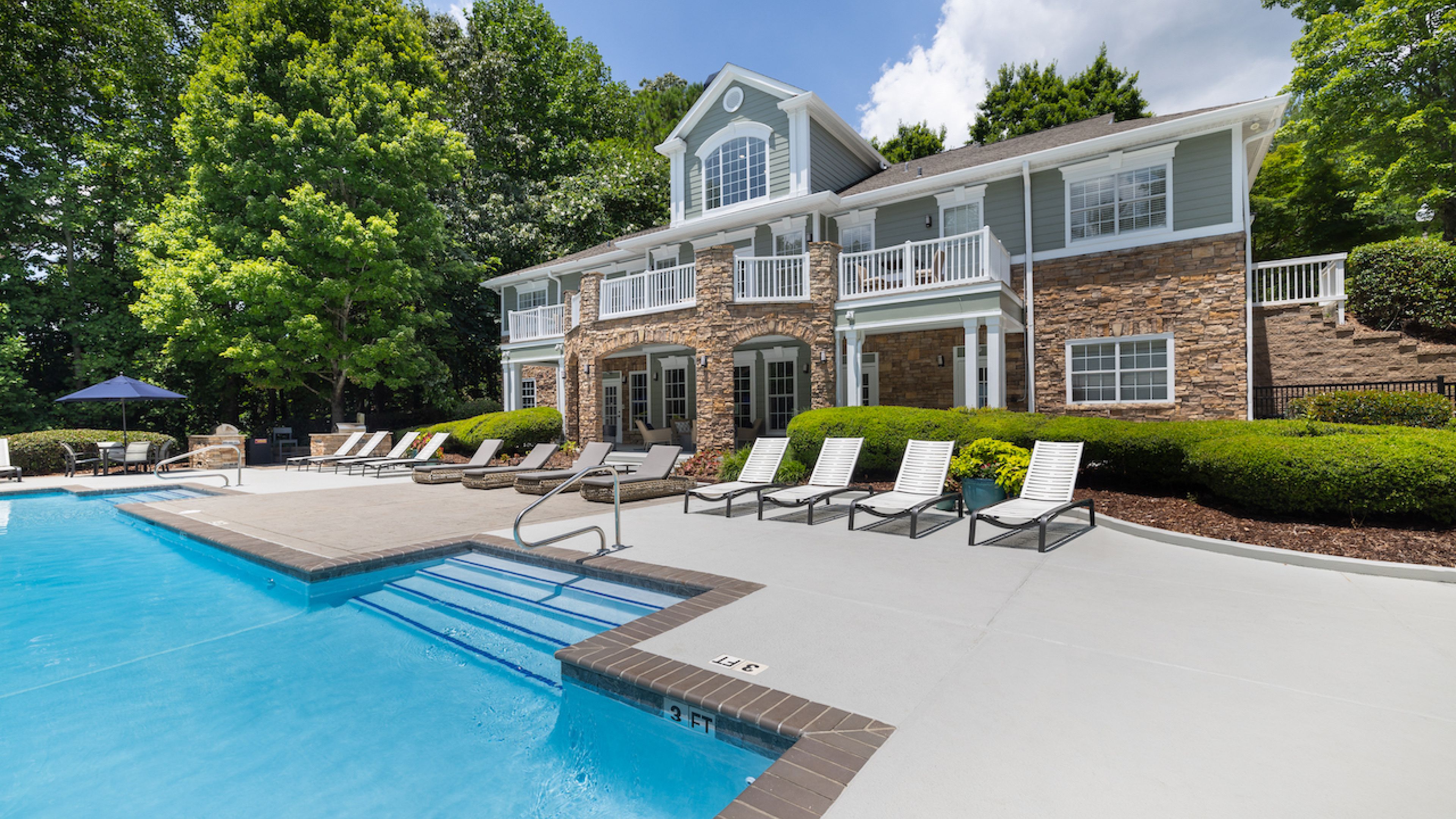 Hawthorne at Lake Heather inviting poolside area with a large pool, lounge chairs, and a beautiful clubhouse set against a backdrop of lush greenery.