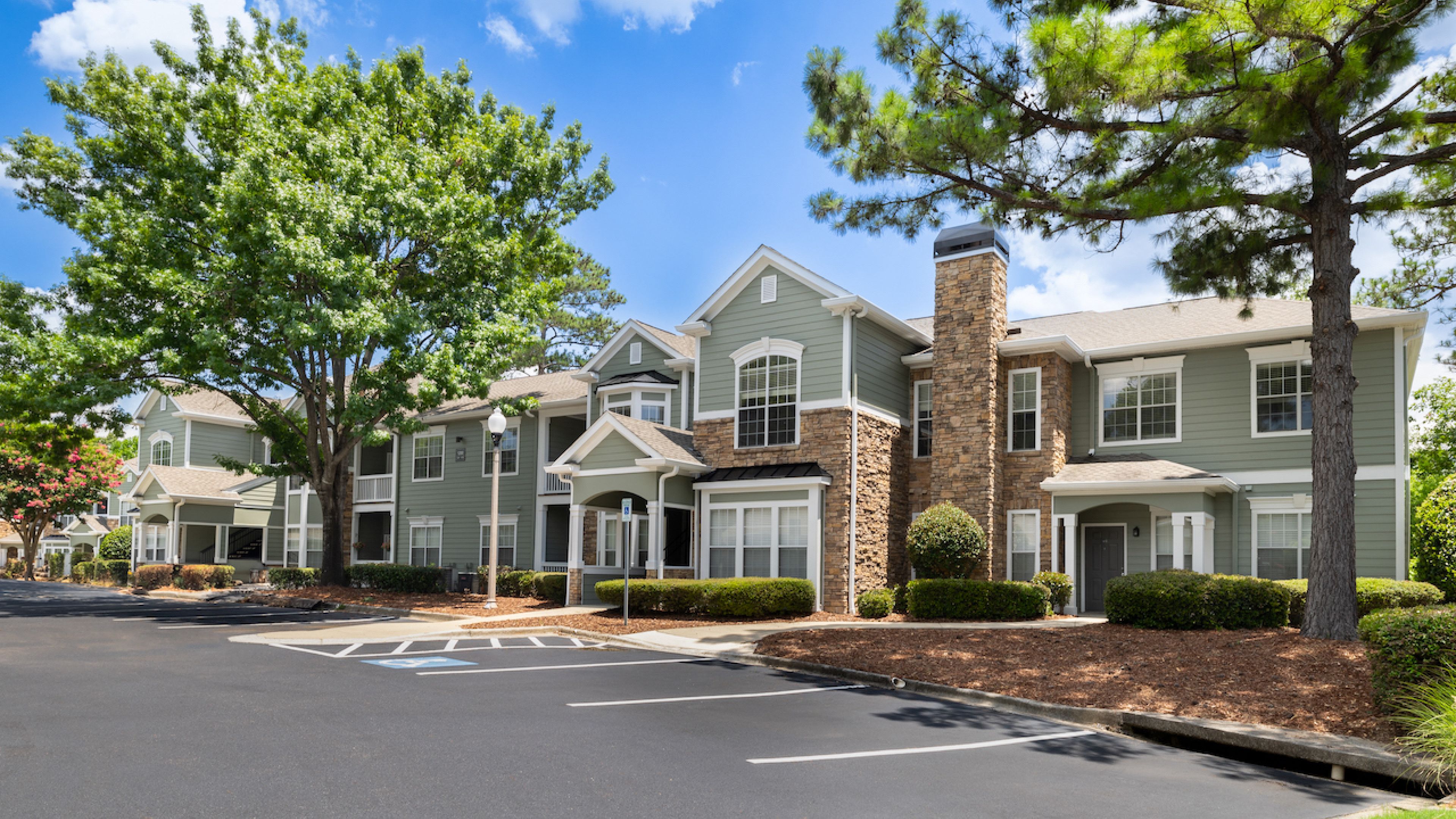 Hawthorne at Lake Heather exterior showcasing its well-maintained buildings surrounded by lush trees and landscaping, with a clear blue sky overhead.